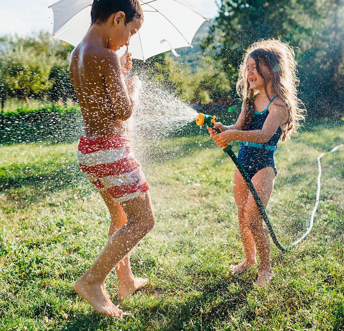 zwei Kinder die im Garten mit einem Wasserschlauch spielen