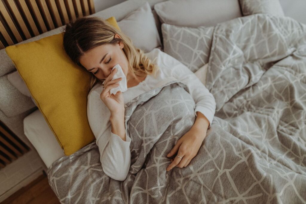 Frau liegt im Bett mit Grippe und putzt sich die Nase.