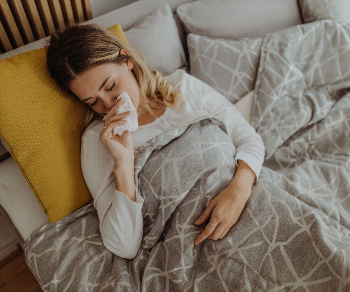 Frau liegt im Bett mit Grippe und putzt sich die Nase.