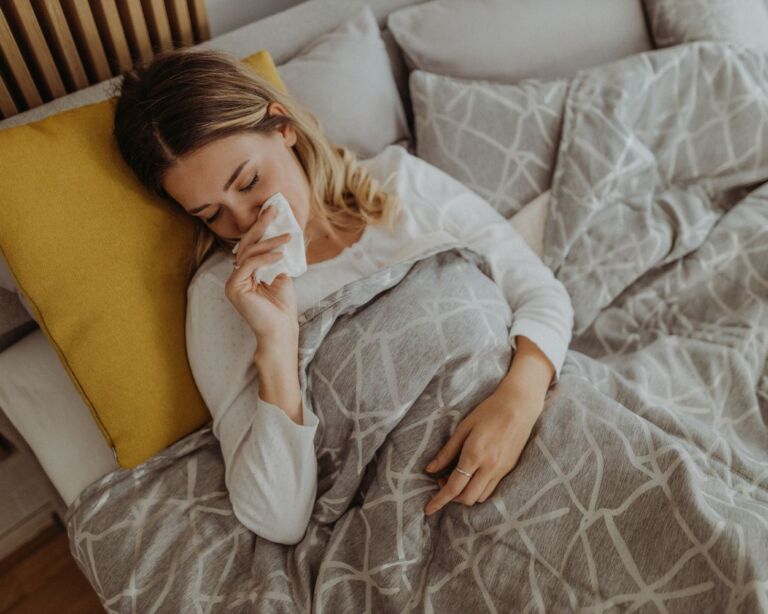 Frau liegt im Bett mit Grippe und putzt sich die Nase.