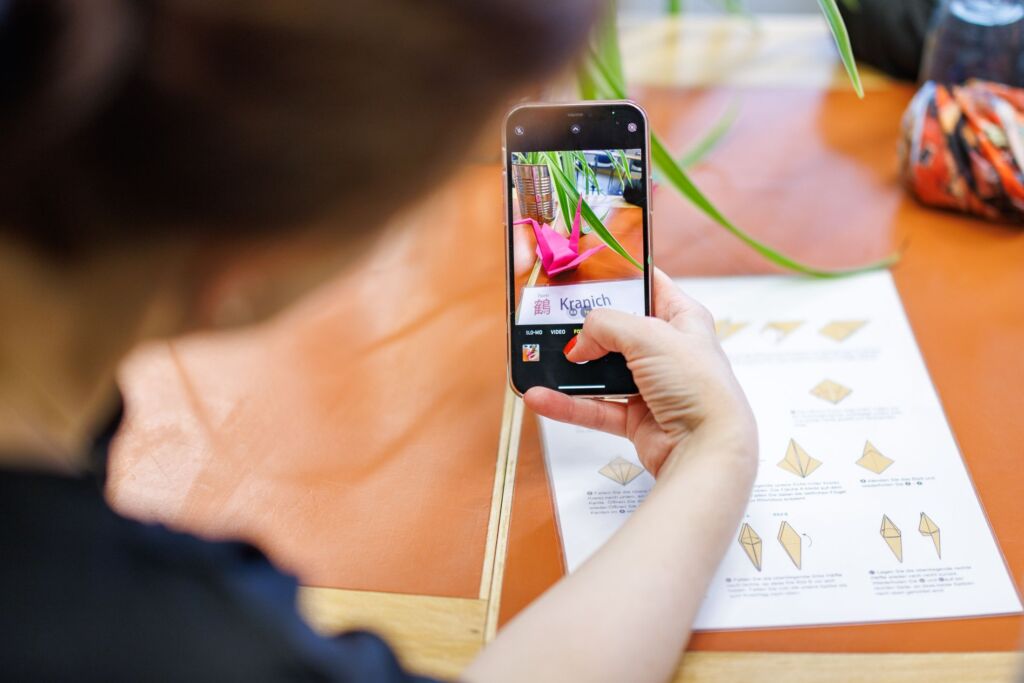 Frau fotografier mit Handy ein Kranich aus Papier